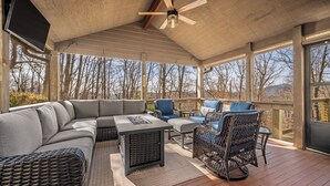 A covered outdoor seating area with a ceiling fan, a flat-screen TV, and a view of trees and mountains. - Scenic Solitude in Lake Lure (Lake Lure)