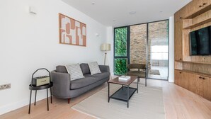 Sala de estar moderna com sofá cinza, mesa de centro, televisão e janela grande com vista para o verde.