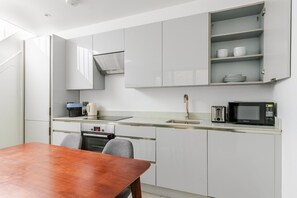 A compact kitchen with white cabinets, a built-in microwave, a kettle, and a small oven. - Blueground | Marylebone, wifi, nr Regent's Park (London)