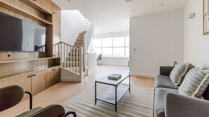 Uma sala de estar moderna com televisão de tela plana, armários de madeira, uma escada e um sofá cinza.