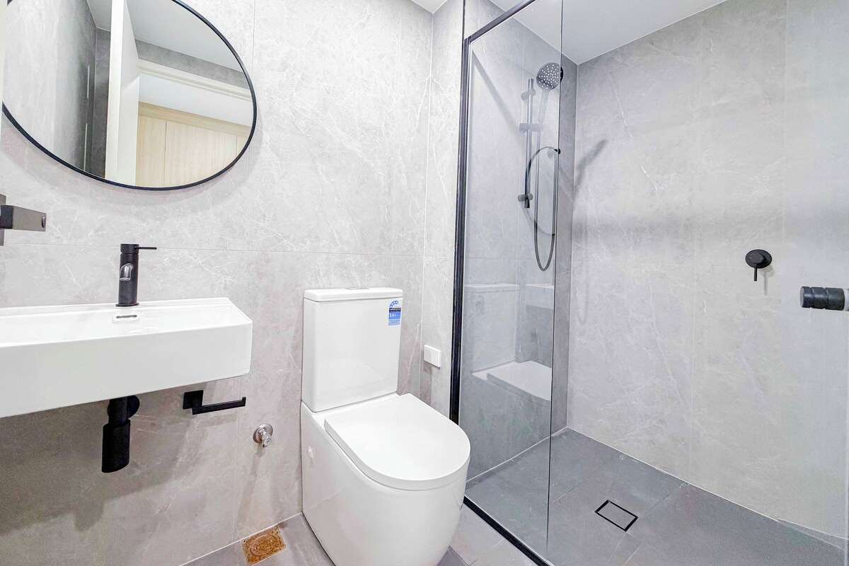 A modern bathroom with a glass-enclosed shower, a white toilet, a sink with a mirror, and a marble wall.