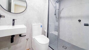 Un baño moderno con ducha envuelta en vidrio, inodoro blanco, lavabo con espejo y pared de mármol.