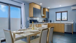 A modern kitchen with a dining area, featuring a large window, a built-in stove, and a dishwasher. - NEW 4BR3.5BA Home w/Private Pool ~ Good Location (Noord)