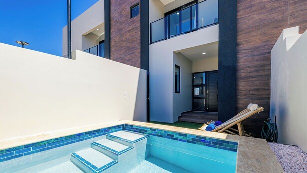 A modern building with a swimming pool, a balcony, and a staircase leading to an upper level. - NEW 4BR3.5BA Home w/Private Pool ~ Good Location (Noord)