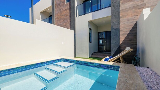 Une piscine ext érieure moderne, avec une zone d’eau d’un bleu limpide, entourée d’un mur blanc et d’une terrasse en bois.