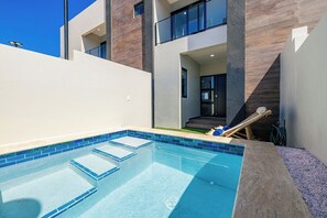 A modern outdoor swimming pool with a clear blue water feature, surrounded by a white wall and a wooden deck. - New 4BR3.5BA Retreat w/Prvt Pool ~ CentralLocation (Noord)