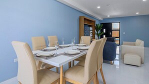 Un coin repas avec une table blanche dressée pour six personnes, entourée de chaises de couleur beige.