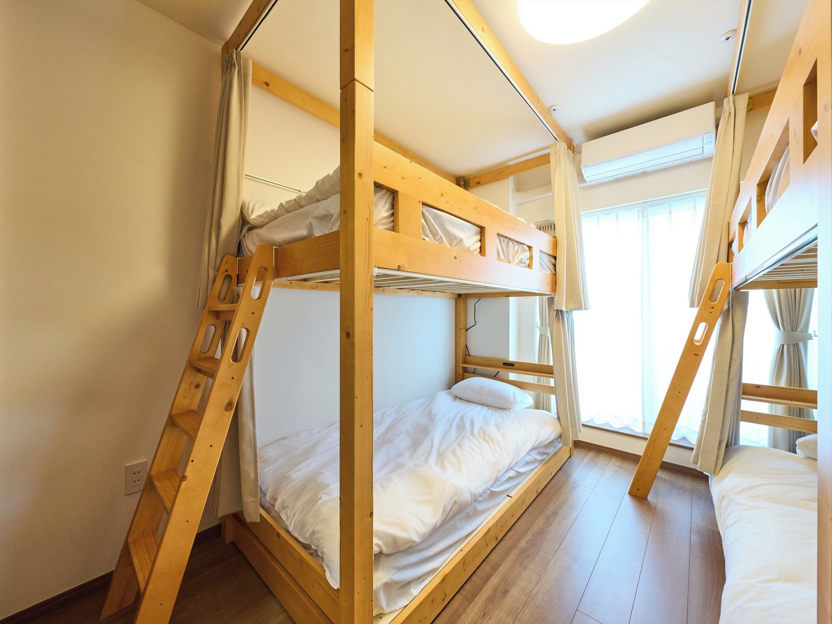 A bunk bed room with wooden frames, a ladder, and a window with curtains.