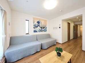 A modern interior with a sofa, a potted plant, and a wall with a Japanese wave painting. - K-Stay TOKYO HANEDA (Tokyo)