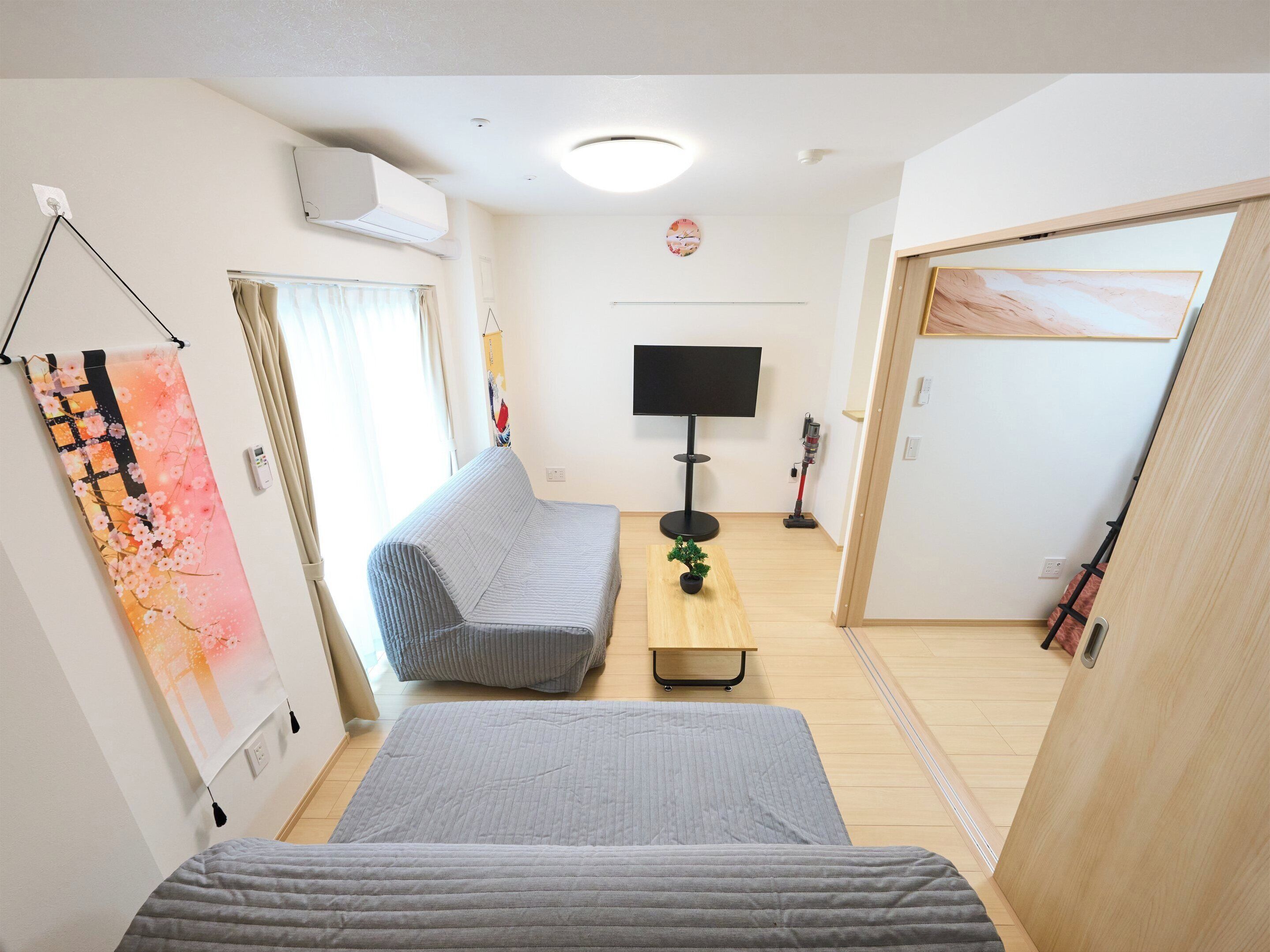 A hotel room with a bed, a sofa, a TV, a small table, and a door.