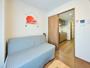 A room with a sofa, a wooden door, a kitchen area, and a wall-mounted artwork. - K-Stay TOKYO HANEDA (Tokyo)