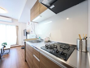 A modern kitchen with a gas stove, stainless steel sink, and wooden cabinets. - K-Stay TOKYO HANEDA (Tokyo)