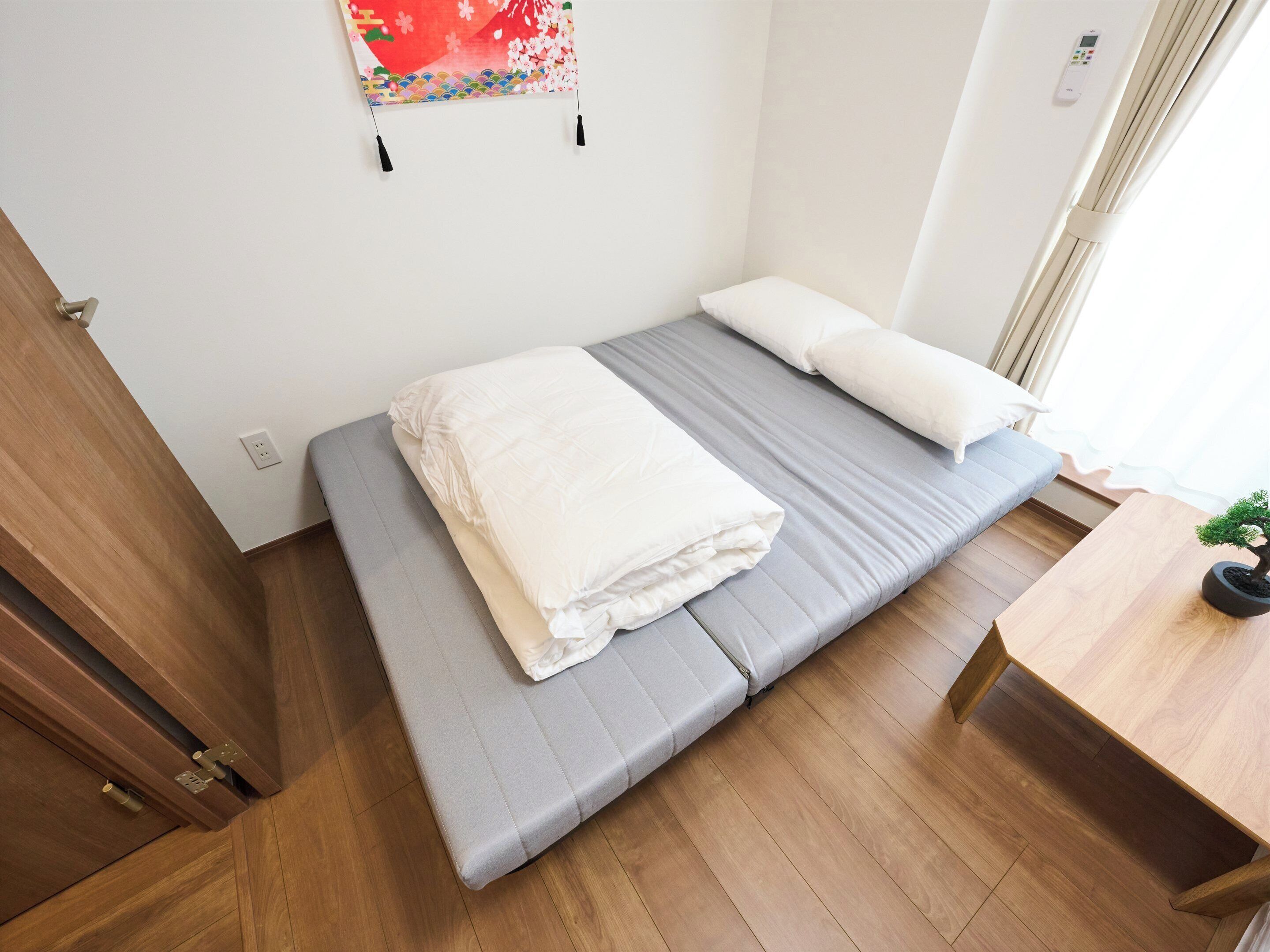 A single bed with grey bedding, a white pillow, and a wall-mounted artwork.