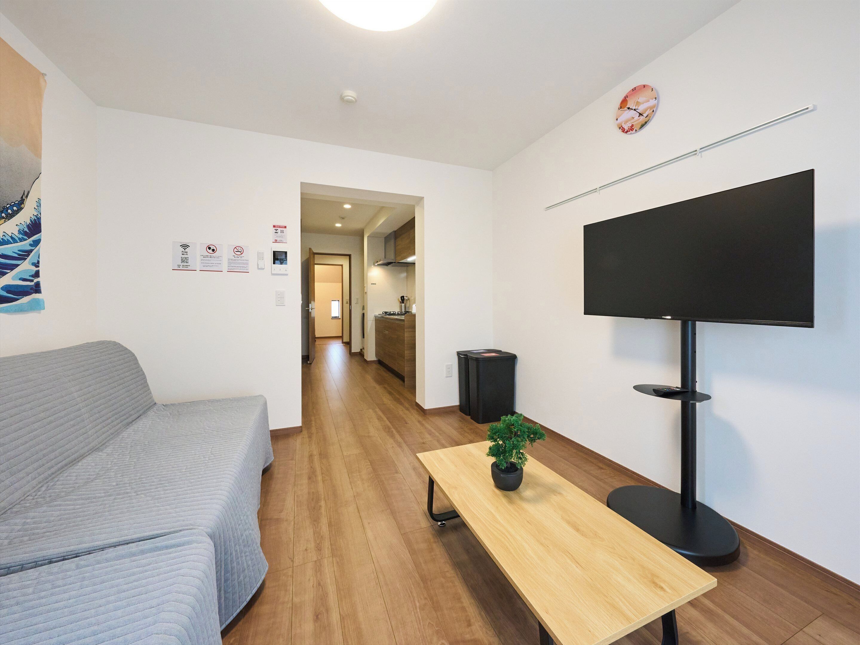 A modern living room with a sofa, a wooden table with a plant, a TV, and a kitchen in the background.