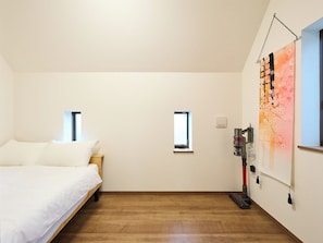A bedroom with a bed, two windows, a painting, and a vacuum cleaner. - K-Stay TOKYO HANEDA (Tokyo)