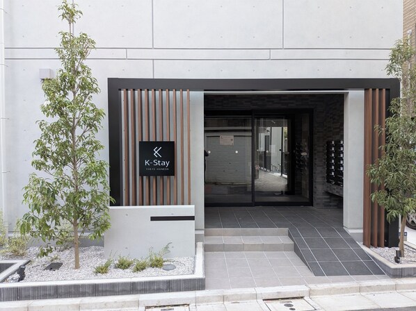 A K-Stay hotel entrance with a modern design, including a signboard, a gated entrance, and a small landscaped area with plants. - K-Stay TOKYO HANEDA (Tokyo)