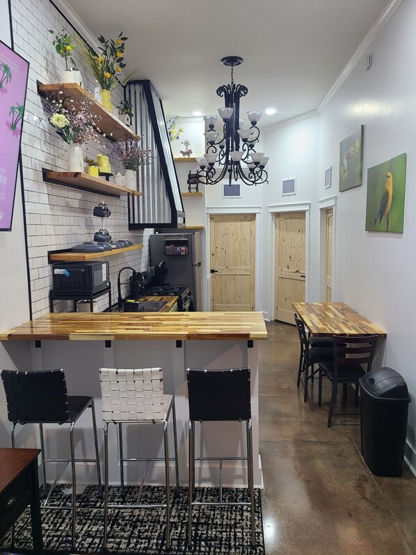 A kitchen with a wooden countertop, black chairs, a black trash bin, and a chandelier.