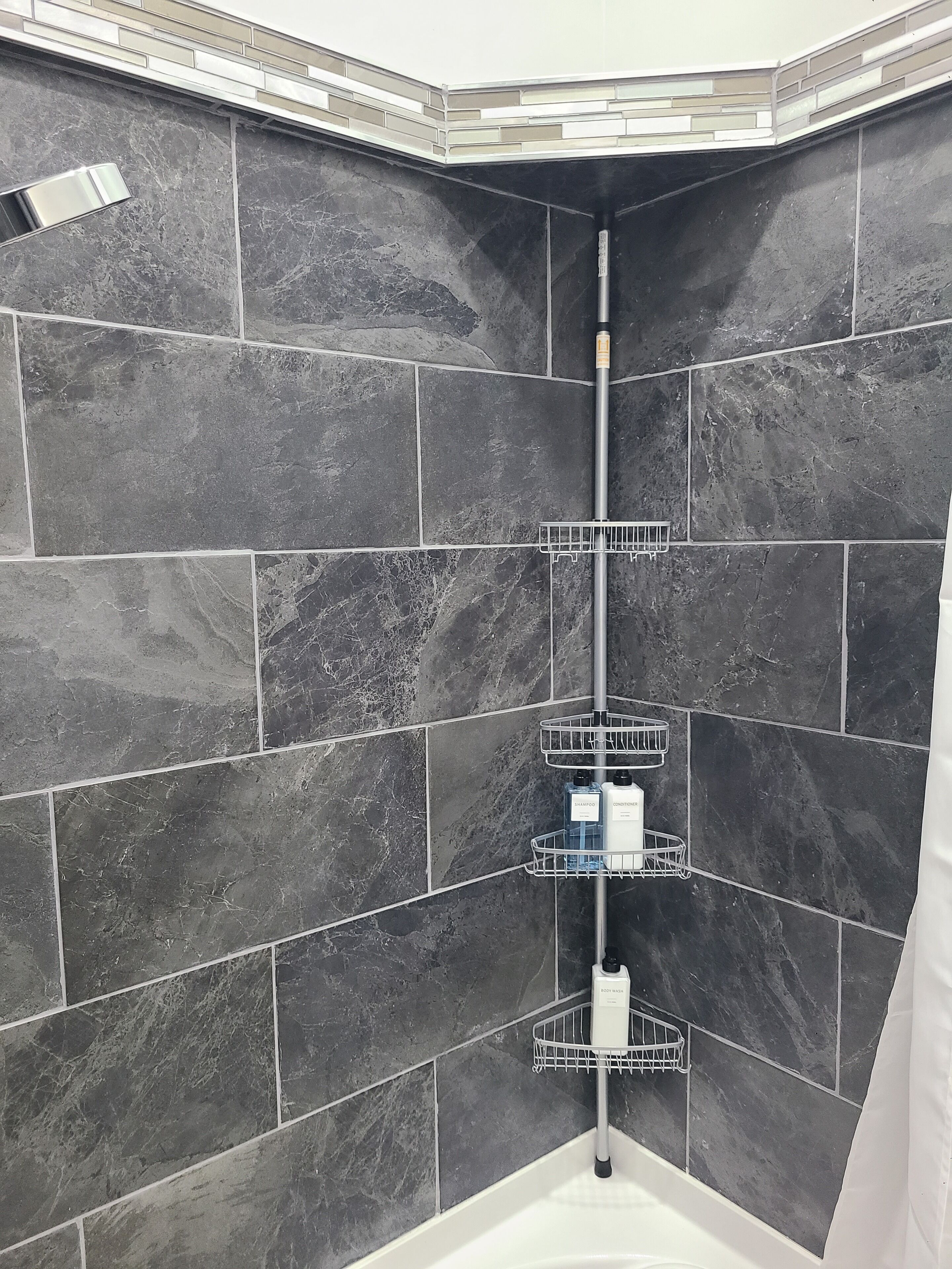 A corner shower area with dark tiles, a metal rack for toiletries, and a white bathtub.