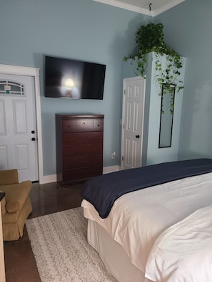 A bedroom with a bed, a dresser, a television mounted on the wall, and a door.
