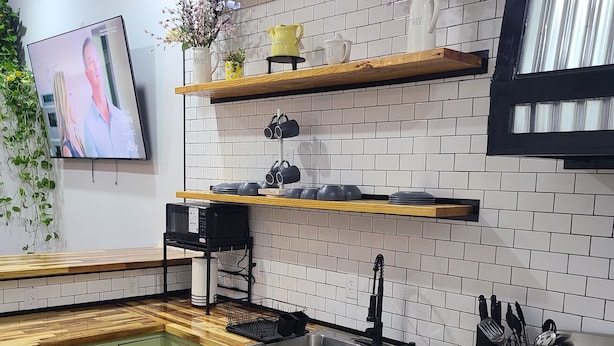 Een keuken met groene kastjes, een houten aanrecht, een roestvrijstalen spoelbak, een kookplaat en een televisie die aan de muur is bevestigd.