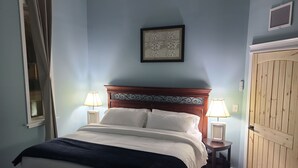 Een slaapkamer met een bed, twee nachtkastjes met lampen, een ingelijst schilderij aan de muur en een houten deur.