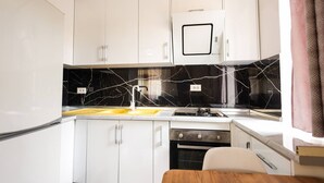 Une cuisine compacte avec des meubles blancs, un pare-feu en marbre noir, un four encastré et un petit coin repas.