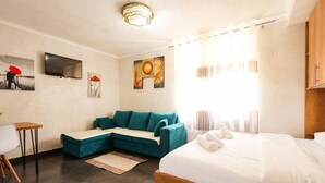 Une chambre d’hôtel moderne, équipée d’un lit, d’un canapé, d’une télévision, d’œuvres d’art accrochées aux murs et d’une fenêtre avec des rideaux.