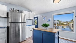 A modern kitchen with a stainless steel refrigerator, white cabinets, a blue island, and a view of a body of water through a large window.