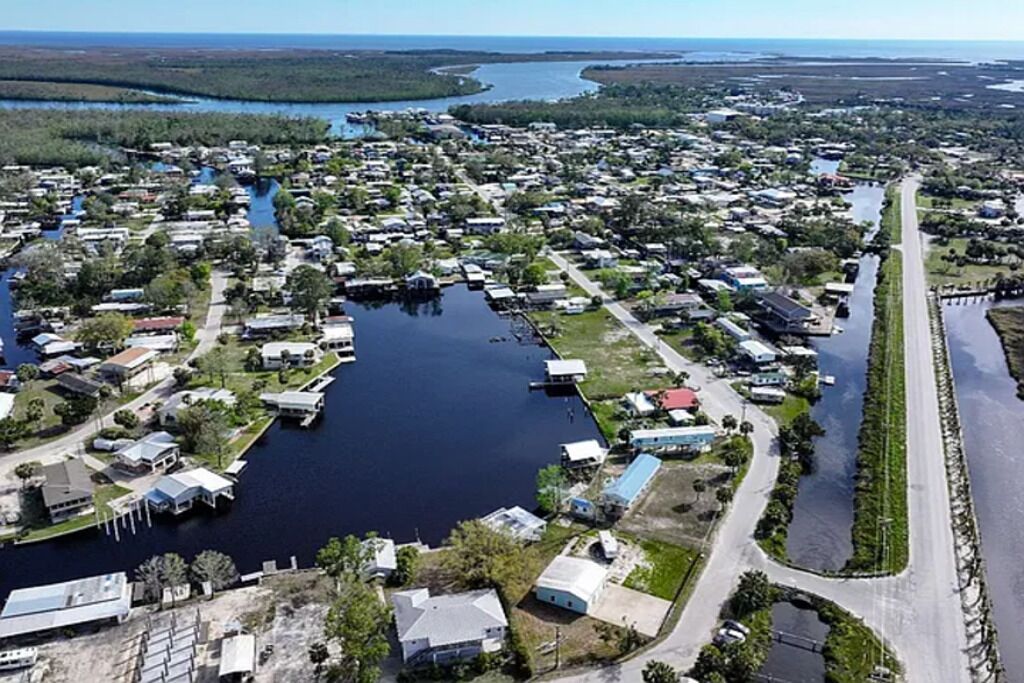 An aerial view of a residential area with houses, a central water body, and a road.