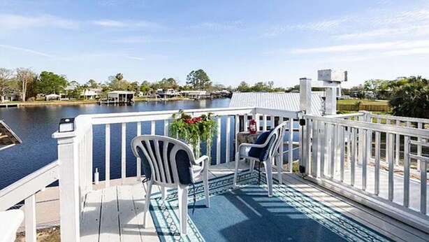 A deck with two chairs and a table, overlooking a body of water and a row of buildings.