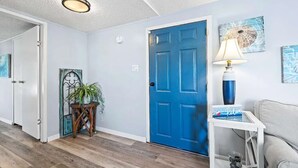 A hallway with a blue door, a white wall, a small table with a lamp, and a potted plant.