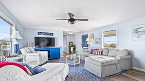 A living room with a ceiling fan, a TV, a blue cabinet, a beige sofa, and a patterned rug.