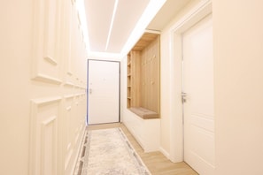 Un couloir étroit, avec une porte blanche au fond, un banc doté d’un coussin et une bibliothèque intégrée en bois.