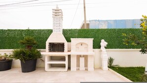 A patio with a white outdoor kitchen, potted plants, and a statue. - Villa Royale in Durr s (Durrës)