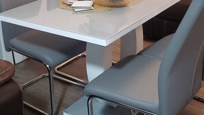 Een eetgedeelte met een witte tafel, blauwe stoelen, een vaas met bloemen en een schaal fruit.