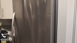 Een koelkast van roestvrij staal in een keuken met lichte kastjes en een houten vloer.