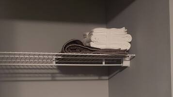 A corner of a room with a grey wall and a metal shelf holding folded towels.
