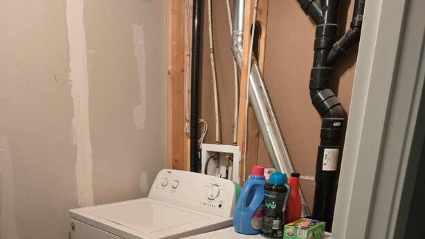 Een wasserij met een voorlader wasmachine en droger, een warmwaterboiler en diverse schoonmaakmiddelen op het aanrecht.