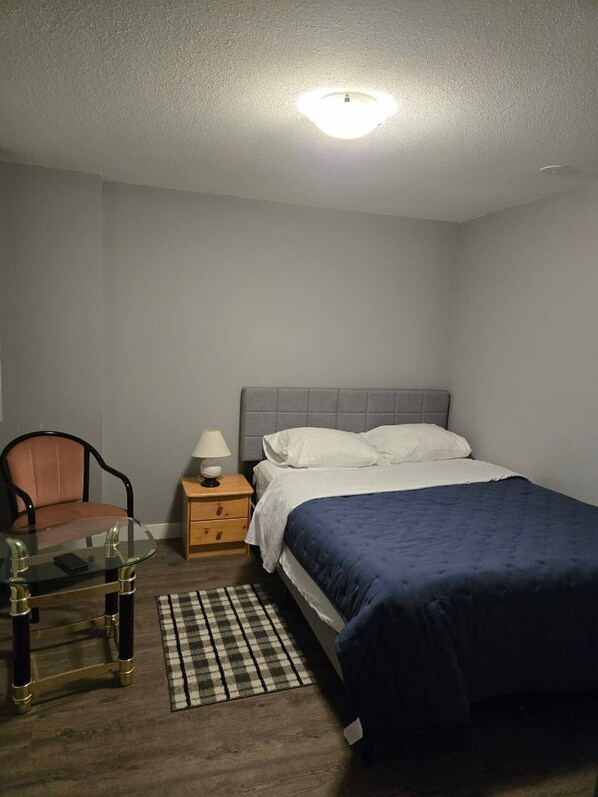 Ein Schlafzimmer mit einem Bett, einem Sessel, einem Nachttisch und einer Lampe.