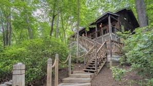 Eine Holzhütte mit einer Treppe, die zu einer Terrasse führt, umgeben von dichtem Wald.