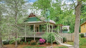 Ein Haus mit Veranda, Treppe und Garten mit Büschen und Baumstumpf.