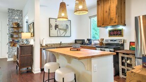 Una cocina con isla de madera, luces colgantes y electrodomésticos de acero inoxidable.