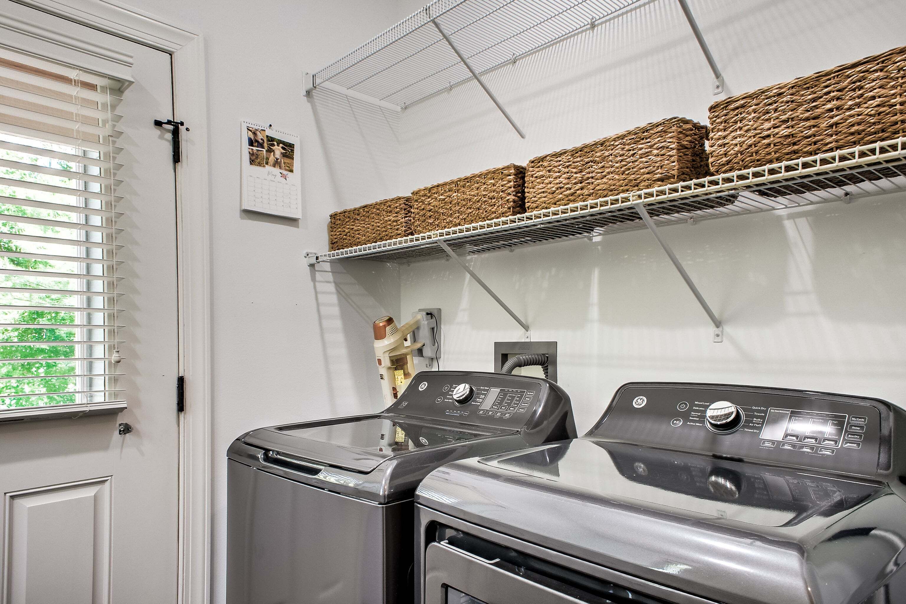 A laundry area with two front-loading washers, a white door, and a window with blinds.