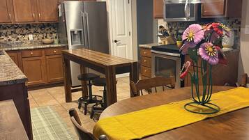A kitchen with wooden cabinets, a stainless steel refrigerator, a dining table with a yellow table runner, and a flower vase.