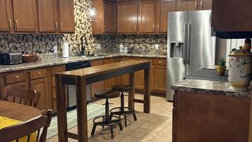 A kitchen with wooden cabinets, a stainless steel refrigerator, a dining table with chairs, and a patterned rug.