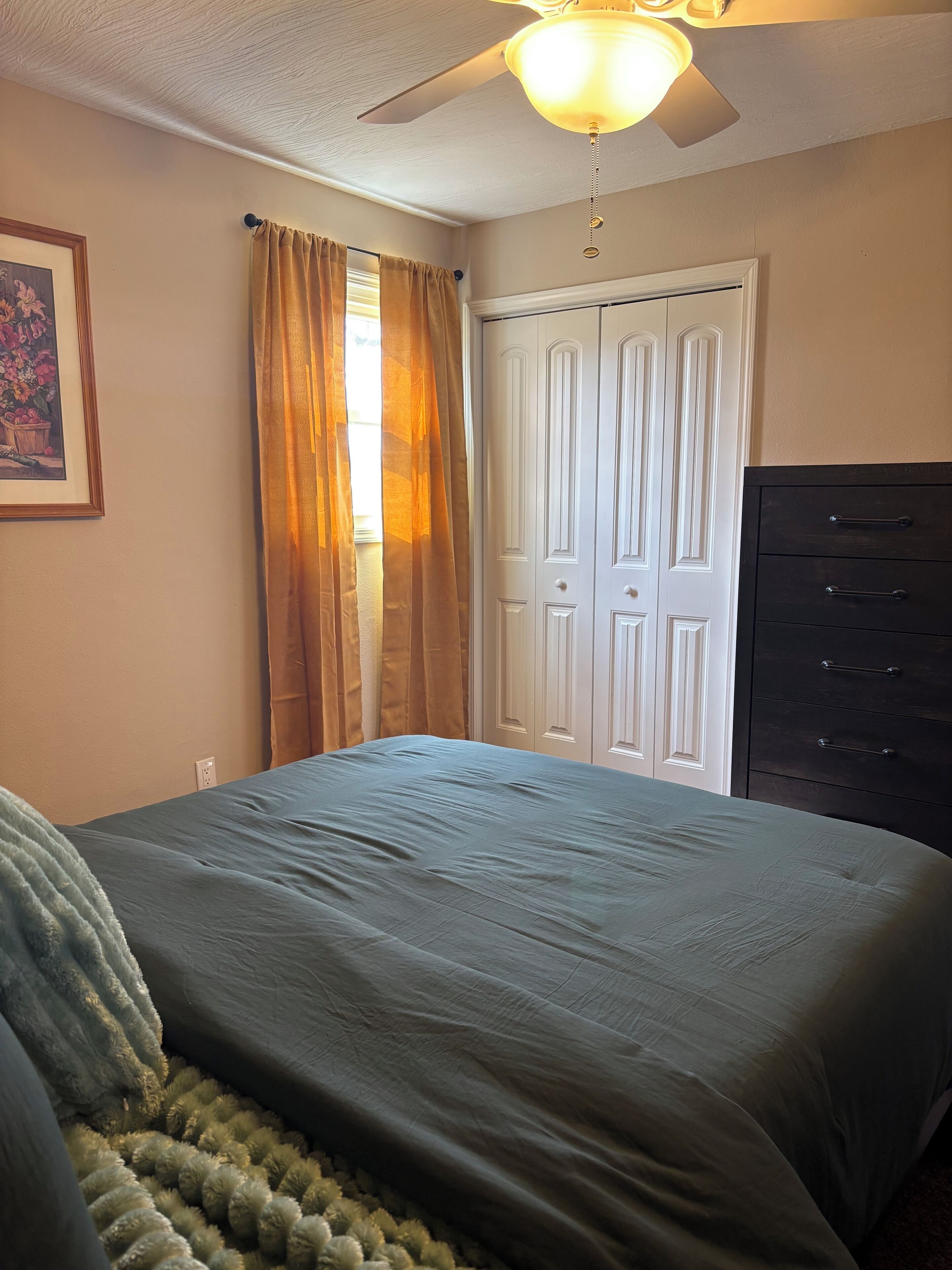 Une chambre à coucher avec un lit, un ventilateur de plafond, une commode et une porte.