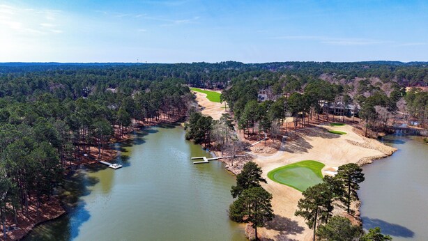 Eine Vogelperspektive auf einen Golfplatz mit einem See, umgeben von dichtem Wald und Wohngebieten.