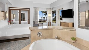 Habitación de hotel con una cama grande, una bañera, un televisor y vistas al exterior.