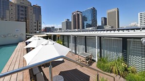 Terraço no telhado com piscina, área de estar externa e vista para o horizonte urbano.