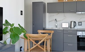 A modern kitchen with grey cabinets, a wooden chair, a potted plant, and a toaster. - Trendy Lifestyle Building 1 Bedroom Secure (Cape Town)